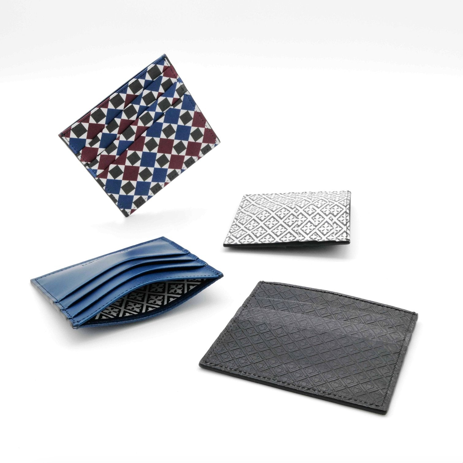 Various slim leather wallets from MARK / GIUSTI’s small accessories collection, arranged artistically to showcase different colours, mosaic patterns, and interior designs.