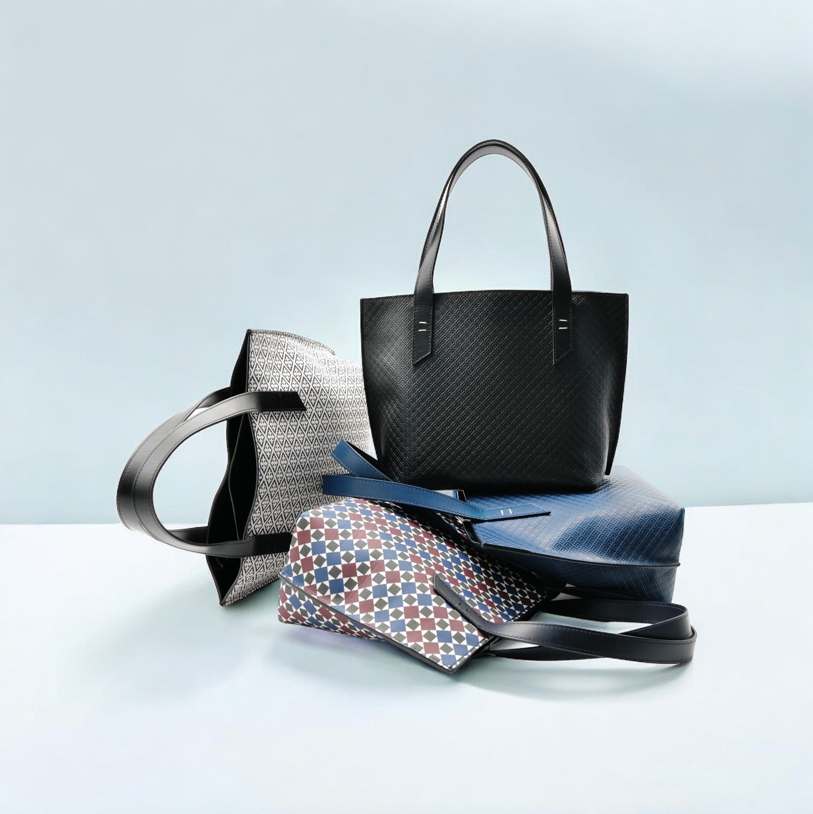 Positano bags from the Amalfi Dreams collection in various colors and mosaic patterns, casually arranged over and next to each other on a minimalist background.