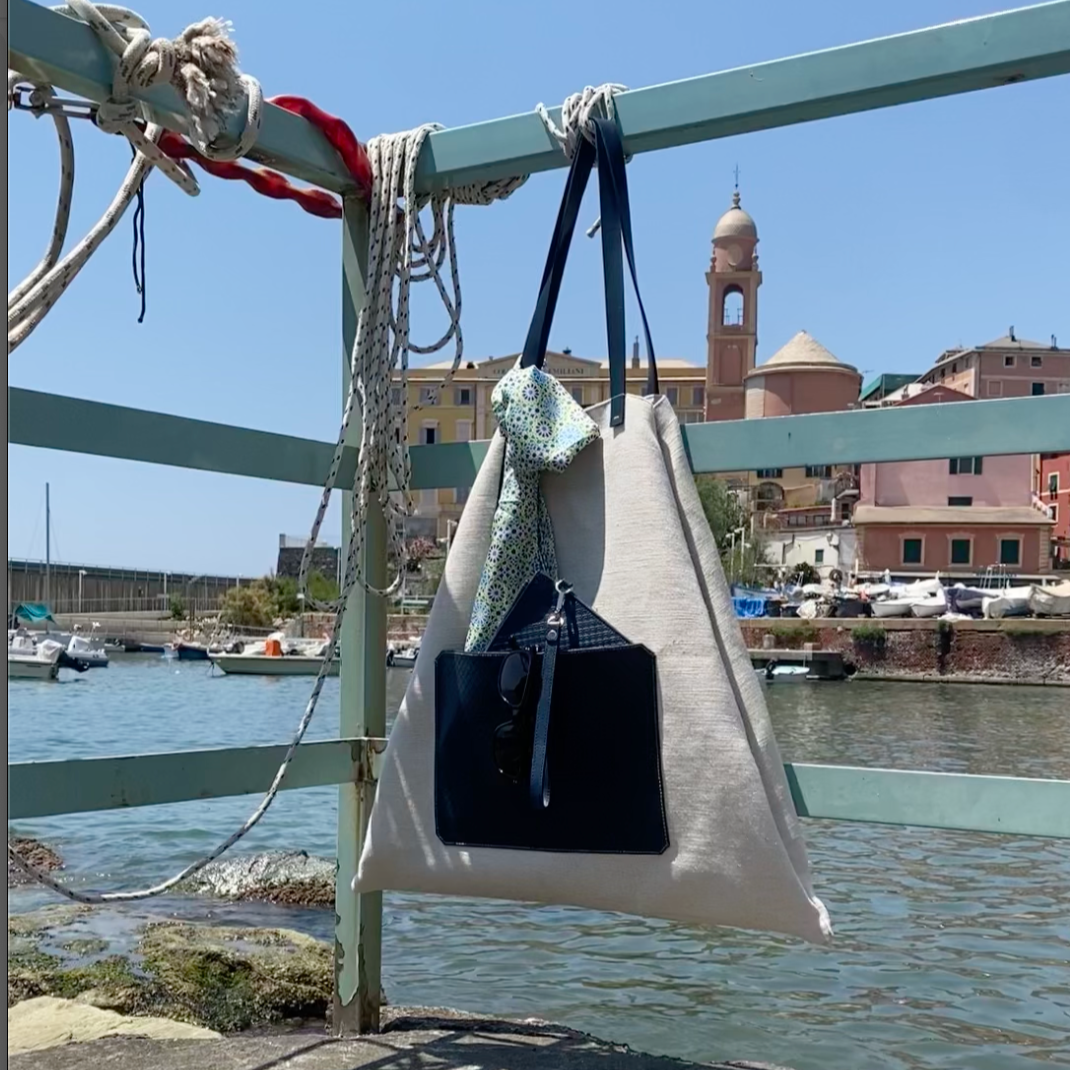 MARK / GIUSTI CALA Beach Tote bag with the Sorrento Crossbody pouch in its front pocket hanging on a railing by a waterfront pier