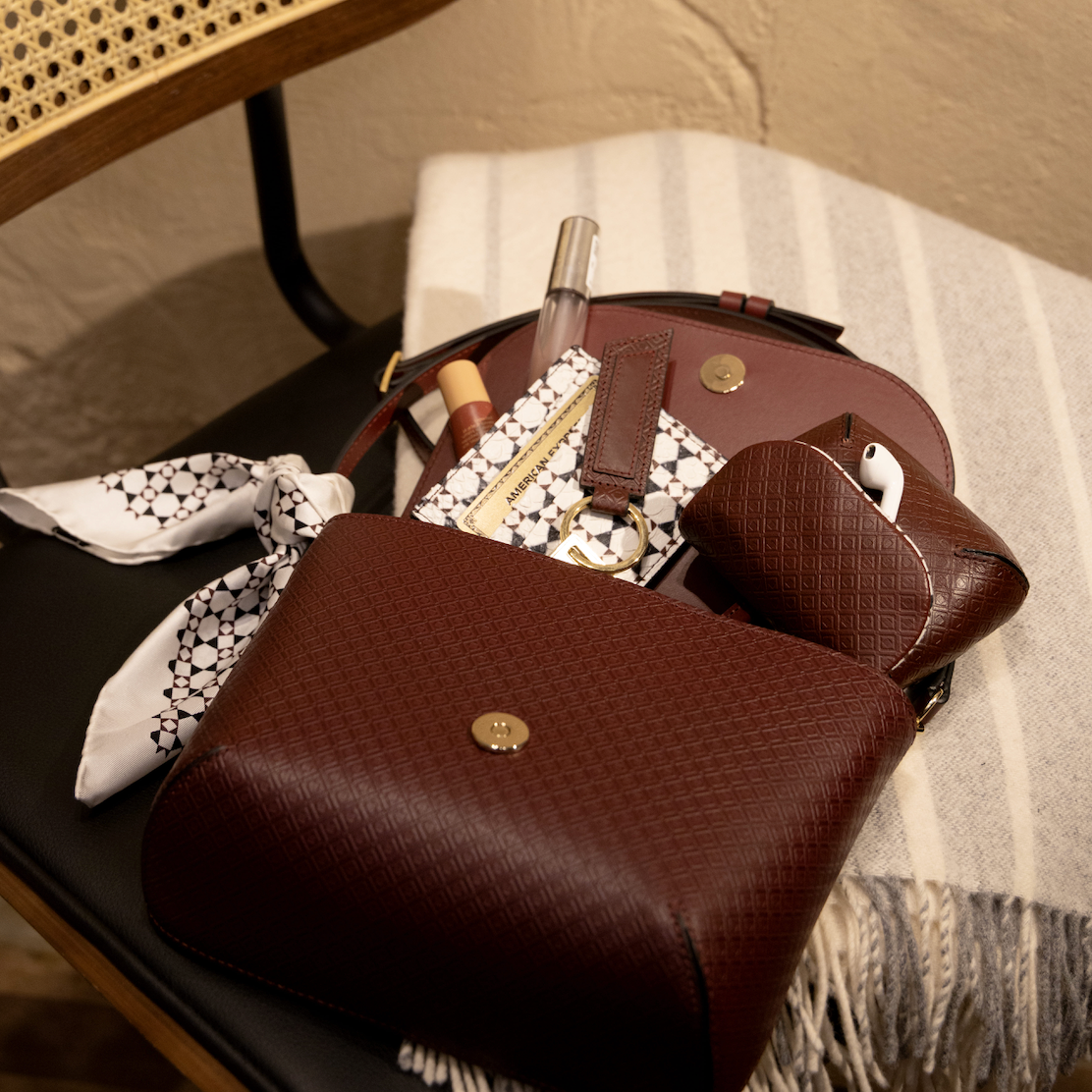 Mark/Giusti Bellagio Cross Body leather bag open on a chair with handcrafted accessories and items peaking out of it.